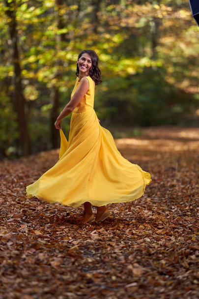 gelukkig jong vrouw in lang geel jurk dansen in een herfst landschap - Foto, afbeelding