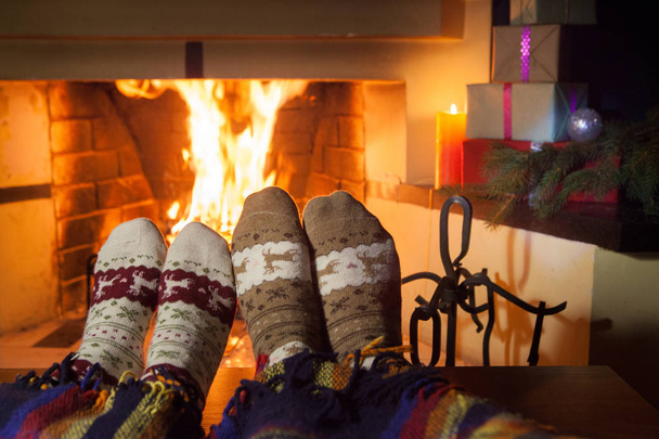 Man and woman in warm knitted socks with cups of hot punch in front of the fireplace - Fotoğraf, Görsel