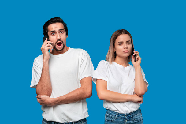 Blond woman and brunet man in white tees and blue jeans are surprised talking on the phone. - Photo, Image