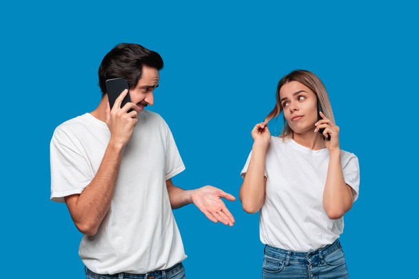 Blond woman and brunet man in white tees and blue jeans are talking on the phone. - Foto, afbeelding