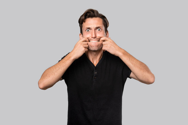 Hombre en una camiseta negra estirando los labios en una sonrisa artificial
. - Foto, Imagen