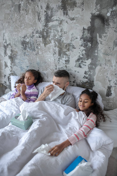 Father lying between daughters while sneezing and coughing - Foto, Imagem
