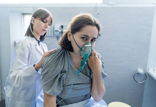 Young sick woman patient with Oxygen Mask while female doctor listens his chest with stethoscope in hospital emergency room. In Smoking and respiratory diseases and anti tobacco advertising campaign. - Φωτογραφία, εικόνα