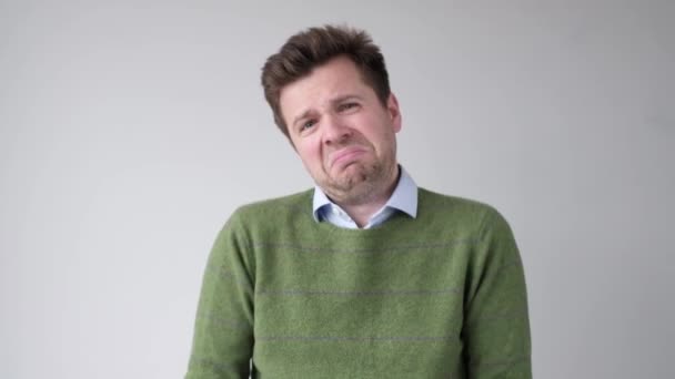 Νεαρός άνδρας που κλαίει με πράσινο πουλόβερ πάνω από γκρι φόντο - Πλάνα, βίντεο