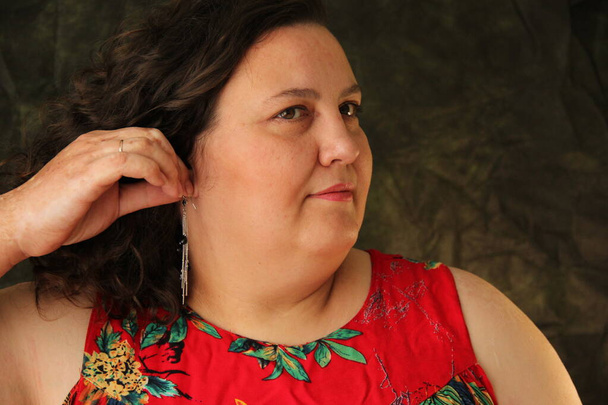 fat woman in a red dress dresses earrings. Model size plus - Foto, Imagen