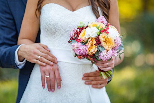 Букет нареченої. Весільна пара тримає руки. Наречена і наречена руки з обручками і весільна сукня
 - Фото, зображення