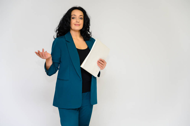 Portrait of a pretty brunette woman with long curly hair on a white background in a business suit with a folder in her hands. He stands in front of the camera, smiles, talks in various poses. - Foto, immagini