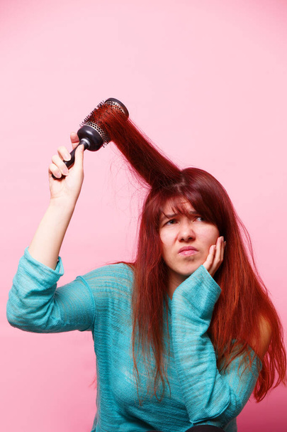 Η γυναίκα βούρτσιζε τα μαλλιά της σε ροζ φόντο. Έννοια της φροντίδας των μαλλιών - Φωτογραφία, εικόνα