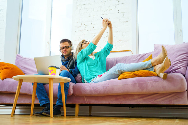Mann und Frau sitzen auf der Couch, unterhalten sich und nutzen Smartphone, Desktop-Computer. Social Media Konzept. - Foto, Bild