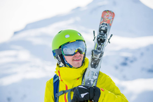 Φωτογραφία του αθλητικού άνδρα φορώντας κράνος με σκι στον ώμο του με φόντο τα βουνά κατά τη διάρκεια της ημέρας - Φωτογραφία, εικόνα