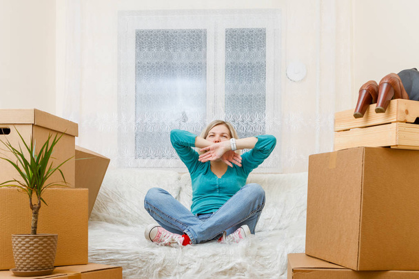 Photo of girl sitting on sofa among cardboard boxes in new apartment - Valokuva, kuva