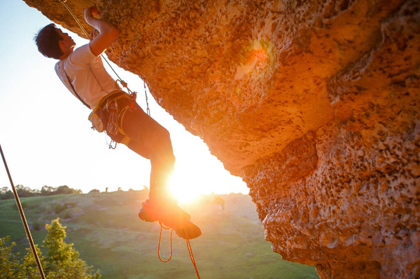 Φωτογραφία ενός άντρα να σκαρφαλώνει πάνω από την πέτρα. Φαινόμενο ηλιακού φωτός - Φωτογραφία, εικόνα