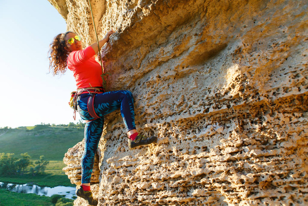 Photo of curly brunette climber climbing on rock at summer day - Photo, Image