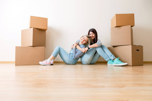 Foto von zwei Mädchen sitzt auf dem Boden zwischen Pappkartons in neuer Wohnung - Foto, Bild