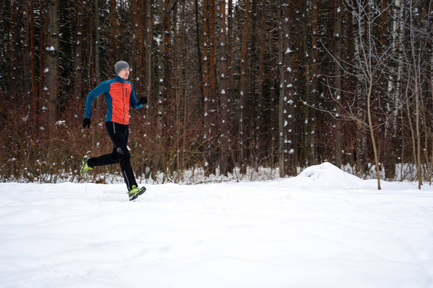 Foto běh sportovec mezi stromy v zimě lese na ranní - Fotografie, Obrázek