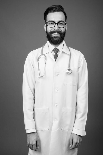 Young handsome bearded Persian man doctor against gray background - Photo, Image