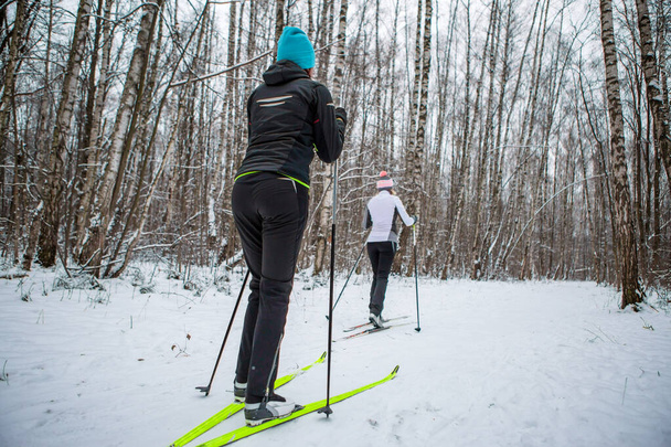 Днем в зимнем лесу катаются на лыжах две женщины и мужчины
 - Фото, изображение
