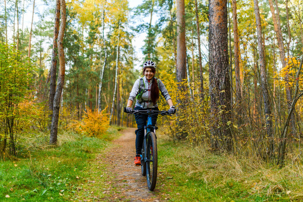 Photo of girl in helmet riding bike in autumn park at afternoon - Photo, Image