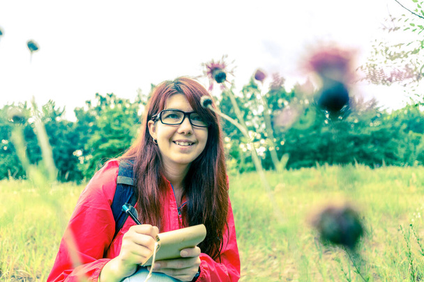 Obrázek bodláku a brunetky s poznámkovým bločkem a tužkou v lese během dne - Fotografie, Obrázek