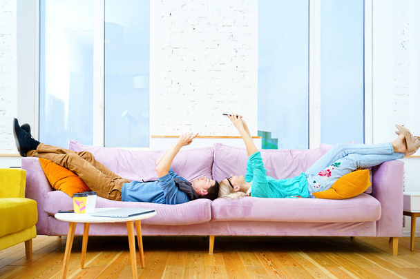 El tipo y la chica están tumbados en el sofá, discutiendo algo en el teléfono inteligente. Concepto de redes sociales
. - Foto, imagen