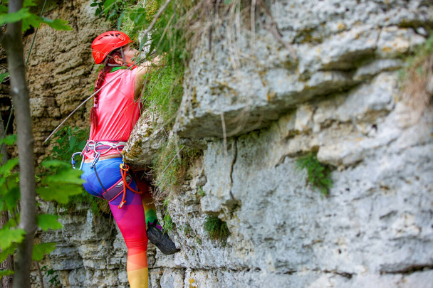Photo from back of sports woman in red helmet climbing up mountain to top at summer day - Photo, Image