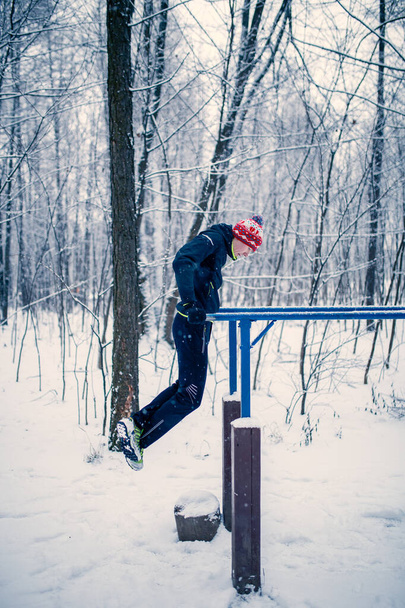 Imagen del deportista en la barra horizontal en invierno en el bosque durante el día
 - Foto, imagen