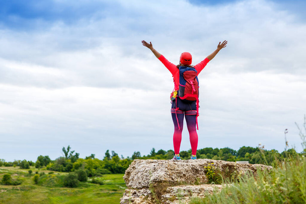 Imagen de la parte trasera del turista femenino con brazos levantados en la colina contra el cielo con nubes y vegetación verde. - Foto, Imagen