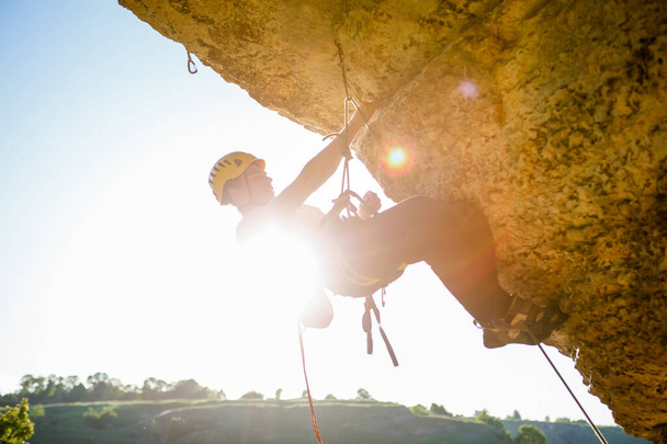 Kuva kiipeilijästä kypärässä kiipeämässä jyrkänteelle. Auringonpurkauksen vaikutus
. - Valokuva, kuva