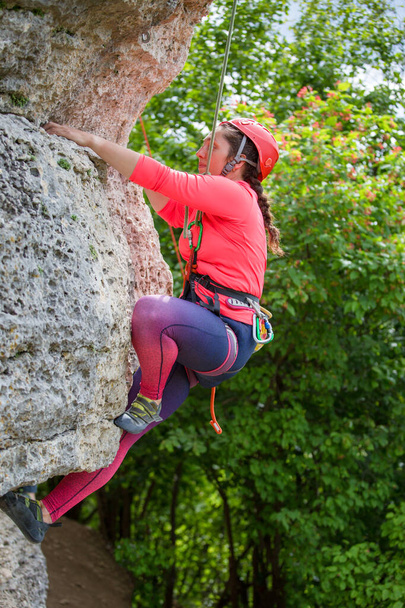 Photo d'une athlète enfilée dans un casque, agrippée à un rocher sur fond d'arbres verts - Photo, image