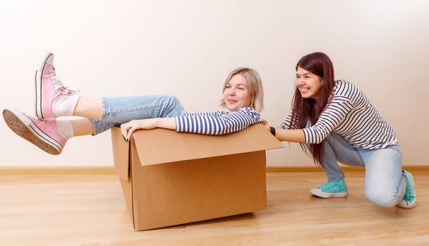 Photo of blonde in cardboard box and brunette in new apartment - Photo, Image
