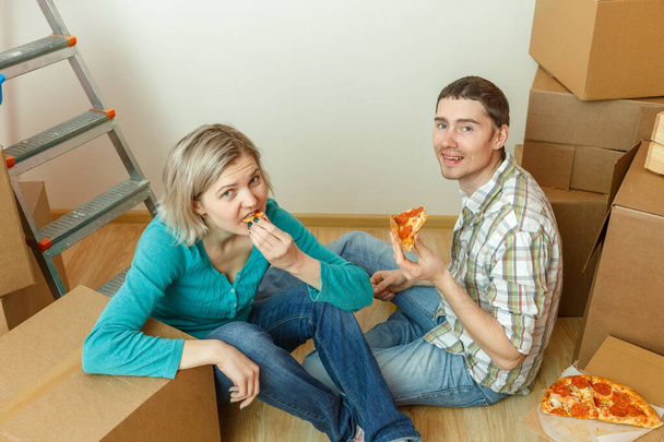 Φωτογραφίες γυναικών και ανδρών που τρώνε πίτσα ανάμεσα σε κουτιά από χαρτόνι στο νέο διαμέρισμα - Φωτογραφία, εικόνα