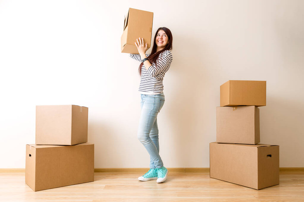 Afbeelding van jonge vrouw tussen kartonnen dozen in nieuw appartement - Foto, afbeelding