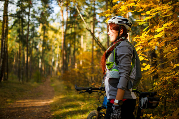 Kuva tyttö kypärä ja urheilu vaatteet polkupyörällä syksyllä metsässä
 - Valokuva, kuva