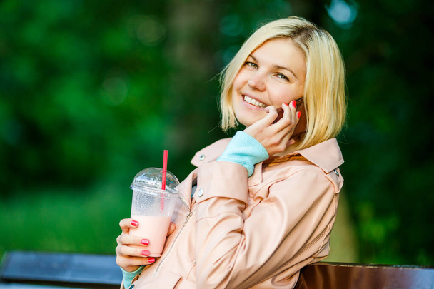 meisje met milkshake praten op telefoon zitten op bank op straat in de zomer - Foto, afbeelding