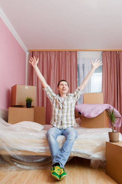 Φωτογραφία του χαρούμενος άνθρωπος κάθεται στον καναπέ ανάμεσα σε κουτιά από χαρτόνι στο διαμέρισμα - Φωτογραφία, εικόνα