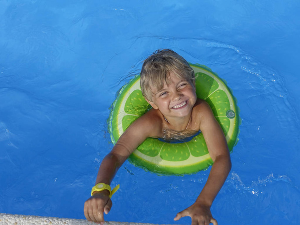 Menino feliz que joga com anel inflável colorido na piscina exterior no dia quente do verão. Criança aprende a nadar
.  - Foto, Imagem
