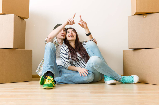 Foto von Mann und Frau auf dem Boden zwischen Pappkartons in neuer Wohnung - Foto, Bild