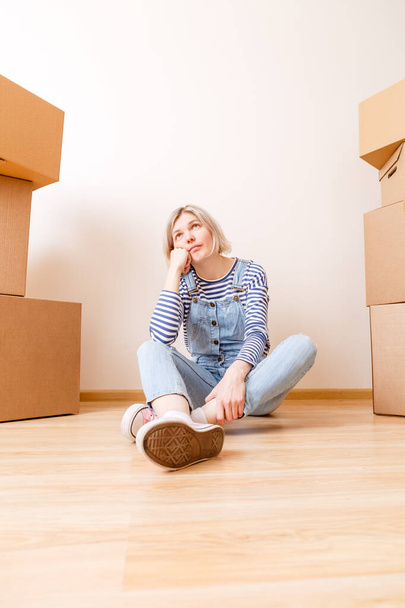 Photo of young woman sitting on floor in empty apartment - Photo, Image