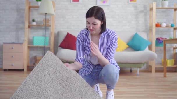 young woman smells a bad smell from the carpet - Materiał filmowy, wideo