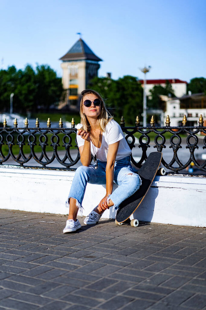 Beautiful and sexy girl sitting on a skateboard and eating ice cream - Zdjęcie, obraz