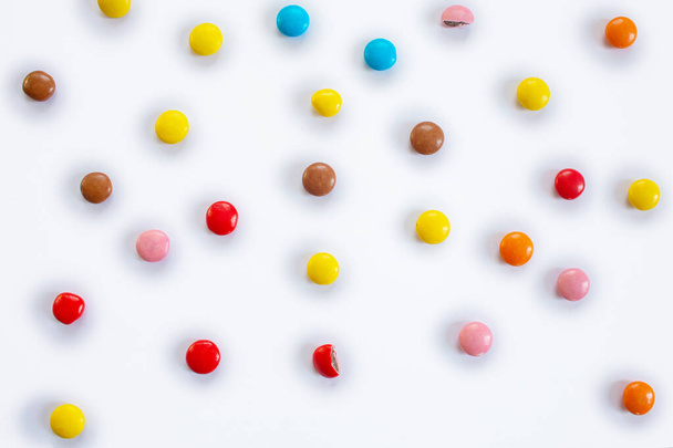 Verspreid veelkleurige kleine ronde snoepjes. Patroon van chocolade dragees in multi-gekleurde glazuur op een witte achtergrond - Foto, afbeelding