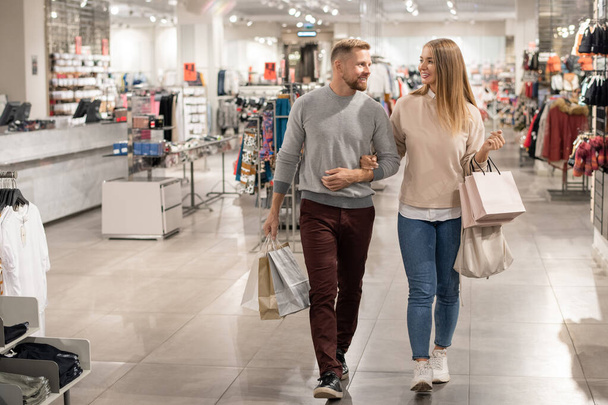 Jovens compradores com sacos de papel deixando o departamento de casualwear depois de comprar roupas novas para ir às compras no shopping
 - Foto, Imagem
