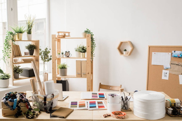 Dřevěný stůl po okně s různými věcmi pro kreativní práci módní nebo interiérové návrhářky v moderním studiu nebo kanceláři - Fotografie, Obrázek