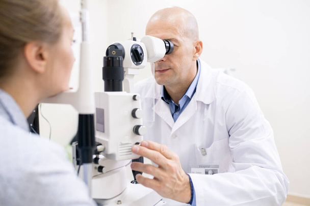 Middle aged professional optometrist checking eyesight of female patient while using new medical equipment - Valokuva, kuva