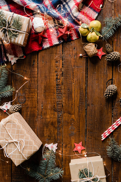 Деревянный фон с обернутыми коробками подарков, гирляндами, рождественскими украшениями, шишками и хвойными
 - Фото, изображение