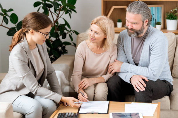 Mature blonde woman listening to young confident real estate agent while going to sign contract in office - Photo, Image