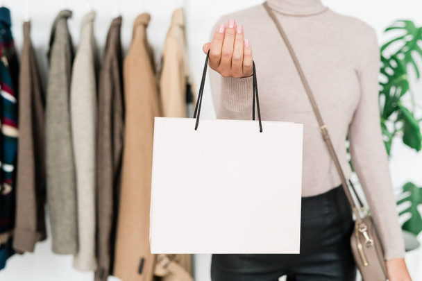 Jonge stijlvolle vrouwelijke shopper met handtas staan in de voorkant van de camera, terwijl het doorbrengen van tijd en geld in boetiek - Foto, afbeelding