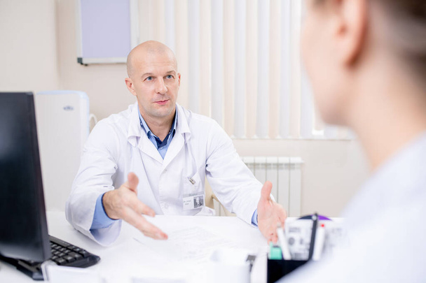Kopasz, magabiztos orvos nézi a beteget, miközben fontos információkat magyaráz vagy ajánlásokat tesz - Fotó, kép