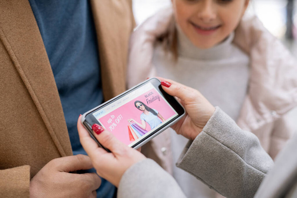 Женщины держат в руках смартфон с домашней страницей интернет-магазина, объявляя о больших сезонных распродажах
 - Фото, изображение
