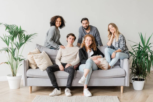 Radosne międzykulturowe nastolatki w ubraniach casualwear relaksujące się na sofie spędzając czas razem w środowisku domowym - Zdjęcie, obraz
